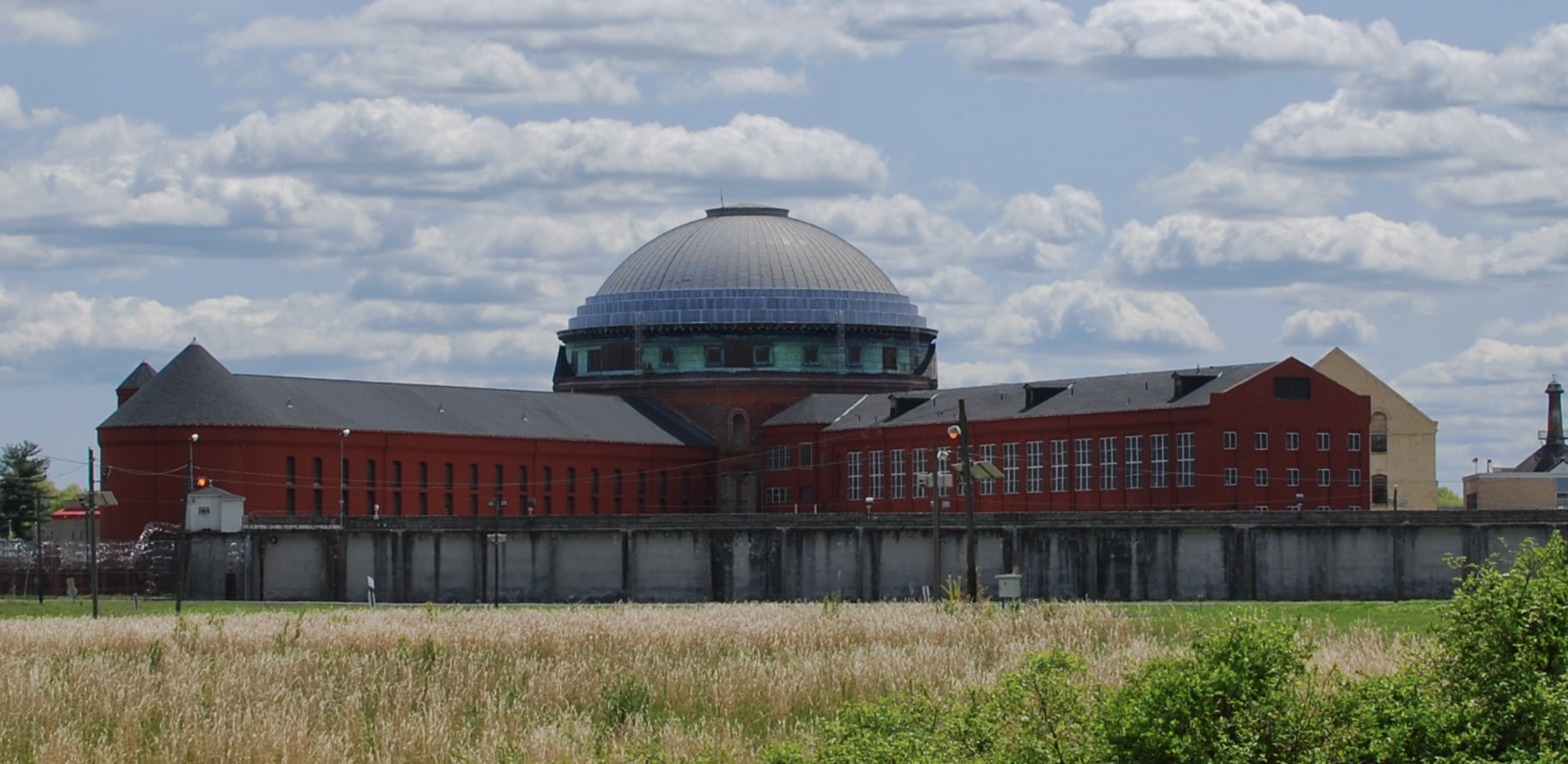 A large correctional facility with a central domed building surrounded by high perimeter walls and security fencing.